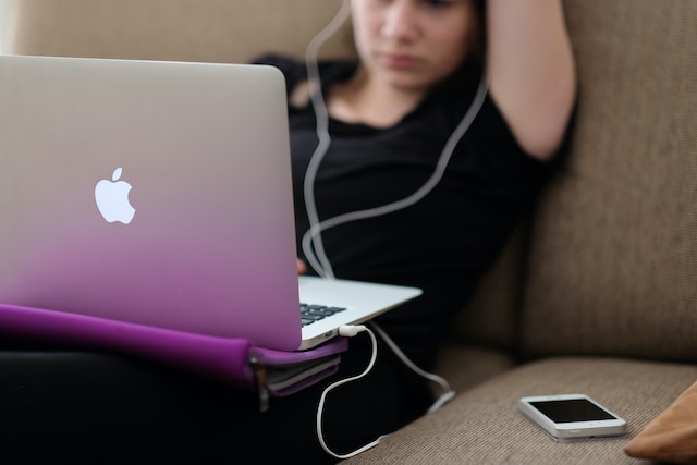 A woman wearing earphones connected to her laptop. 