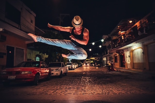 A man performing a high jump while dancing in the street. 