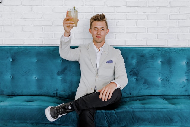 Um homem sentado em um sofá azul levantando um copo. 