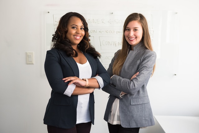 Duas profissionais do sexo feminino em frente a um quadro branco. 