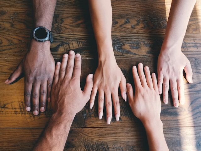 Five people with their hands side-by-side on a table. 