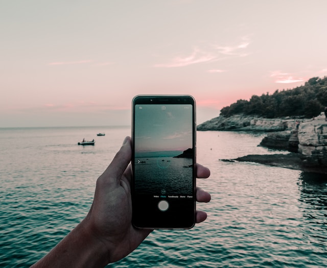 Iemand die een video van de zee maakt met zijn telefoon. 