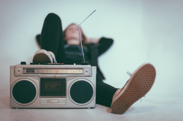 Uma mulher deitada no chão e ouvindo música com um rádio antigo. 