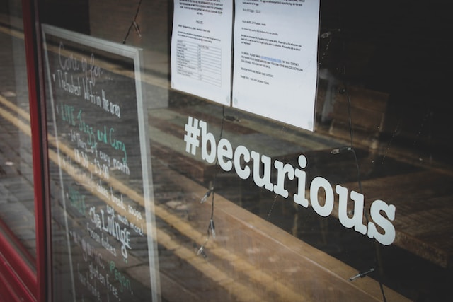 Schild an einem Schaufenster mit der Aufschrift "#becurious".
