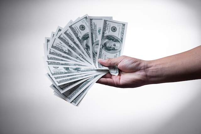A person holding one-hundred dollar bills in one hand.