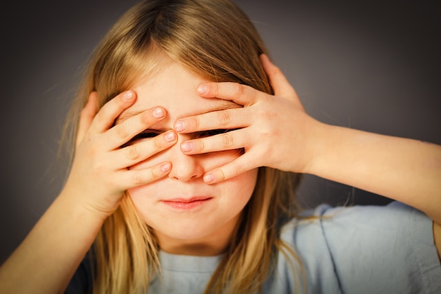 A young girl covering her eyes. 