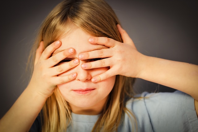 Ein junges Mädchen hält sich die Augen zu. 