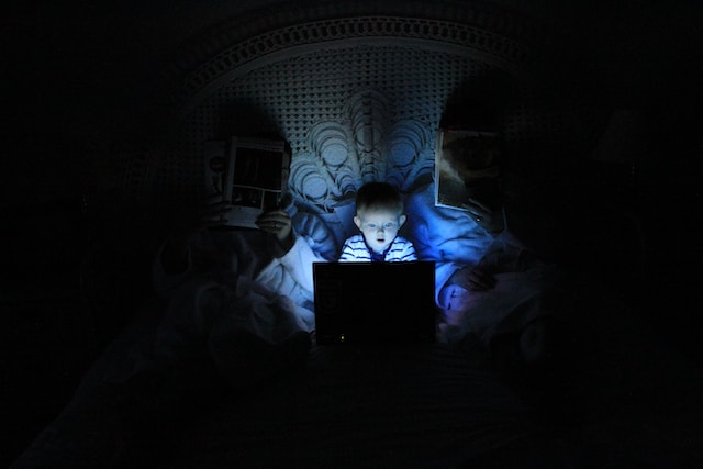 Ein Kind schaut auf einem Laptop, während es zwischen seinen Eltern im Bett sitzt. 