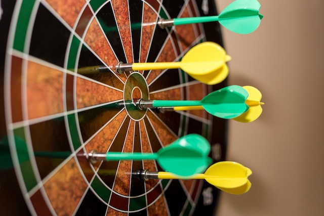 A dartboard with yellow and green darts. 