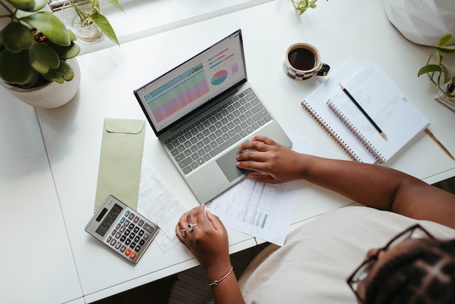 Una persona estudia tablas y gráficos en un ordenador portátil con una calculadora a un lado. 