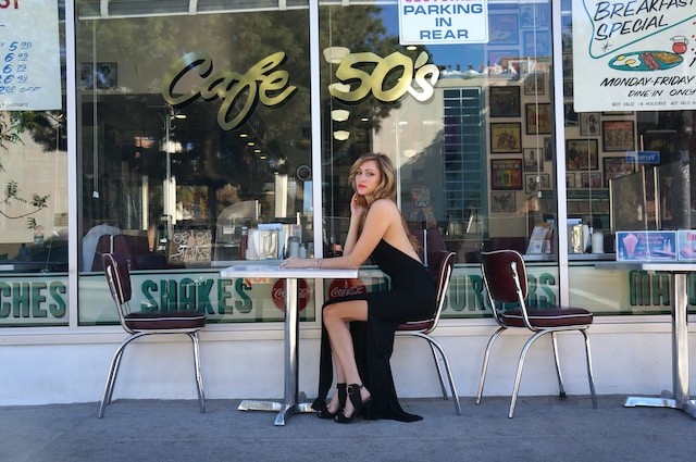 A woman in a long, black dress sitting in front of a cafe. 