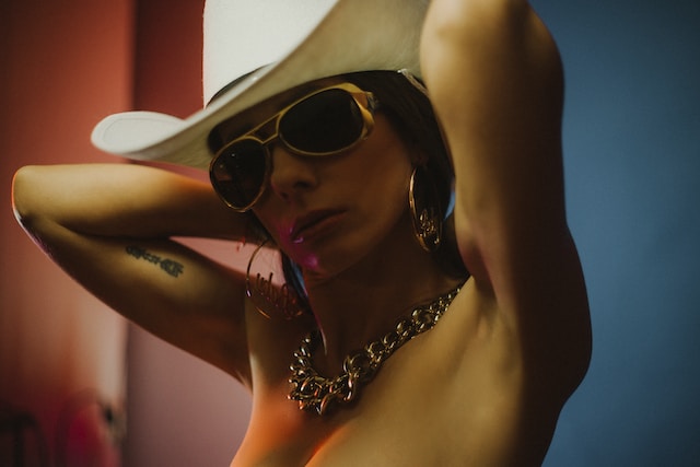A woman wearing a cowboy hat, sunglasses, big earrings, and a heavy chain necklace. 