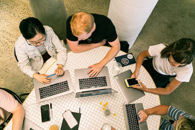 Un gruppo di persone sedute a lavorare sui loro PC e dispositivi mobili.