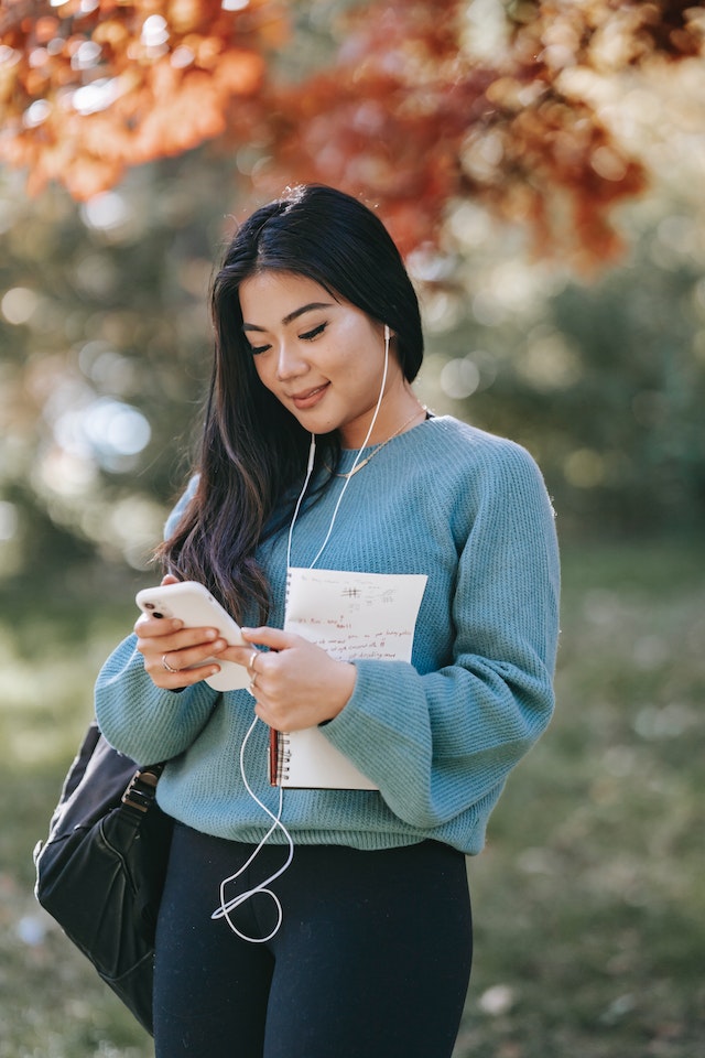 Een jonge vrouw kijkt naar haar telefoon en luistert naar een liedje met een koptelefoon. 