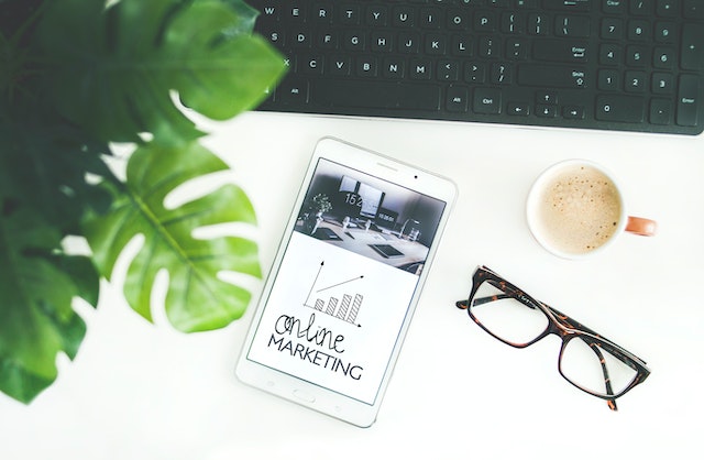 Un téléphone, des lunettes, un clavier et une tasse de café sur une surface blanche.