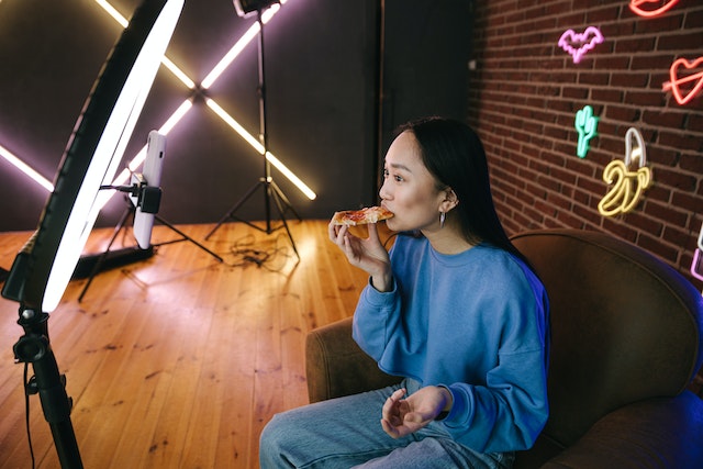 Una chica comiendo pizza y grabando un TikTok.