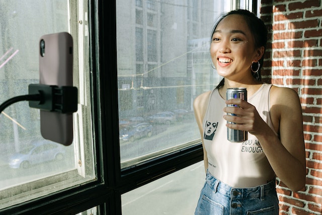 A girl holding a can in front of a smartphone and recording a video for TikTok.