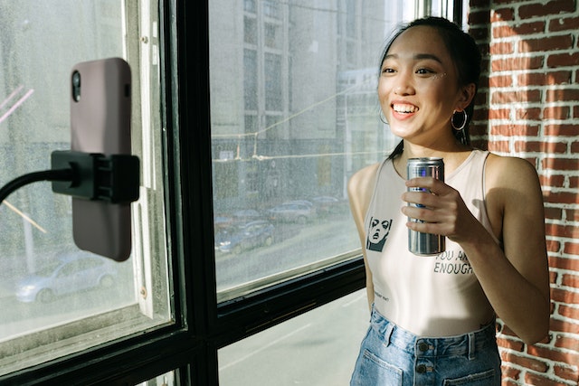 Une femme devant son smartphone se prenant en photo en tenant une boisson énergisante.