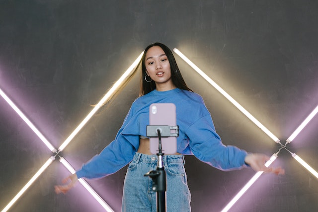 Une femme en pull bleu et jeans dansant devant son téléphone.