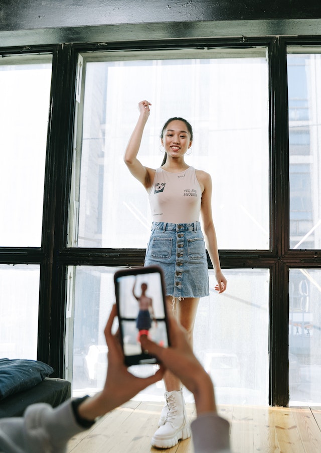 A woman recording a TikTok video, posing in front of a window,