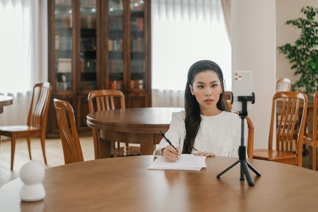 Uma garota sentada em uma mesa gravando um TikTok.