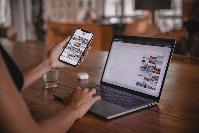 A woman holding her mobile phone and working on her PC to create TikTok content.