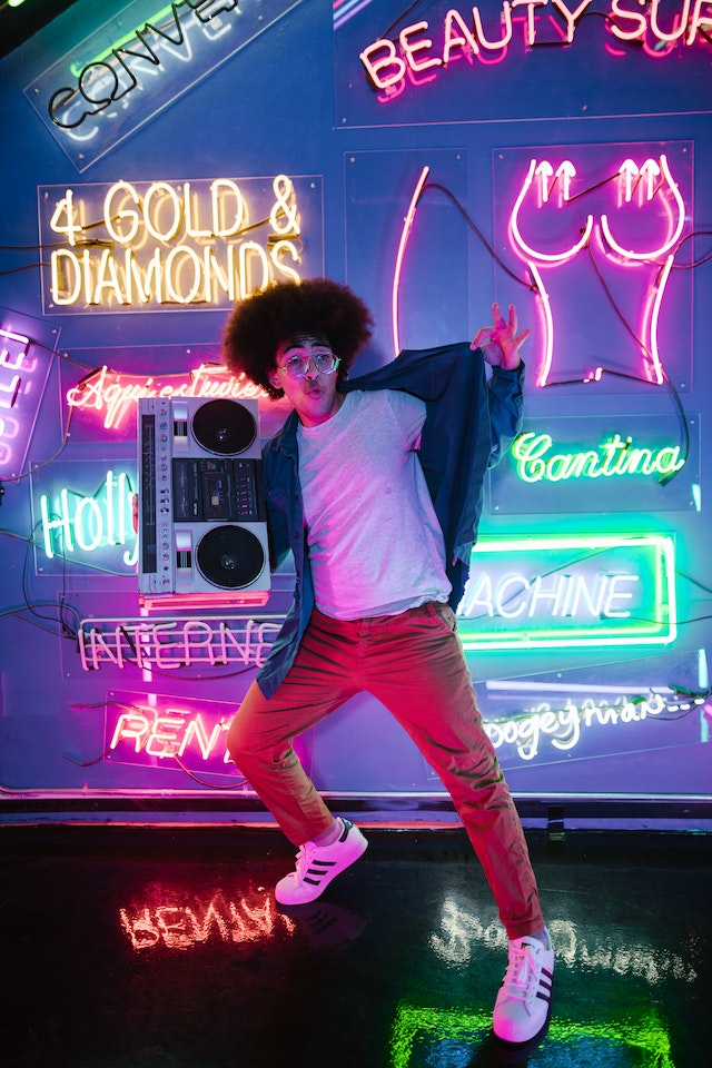 A man holding a cassette player in front of a wall with Neon Lights. 