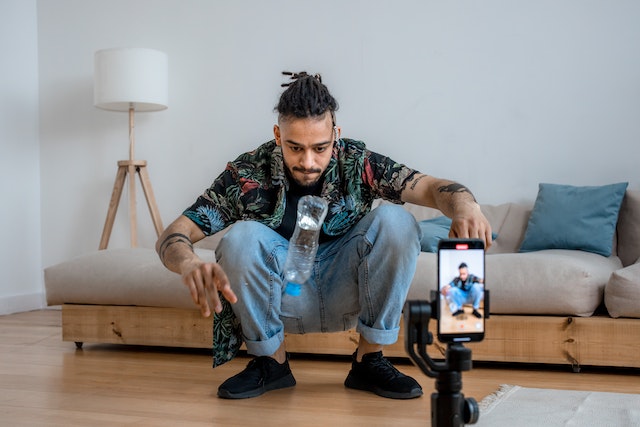 A man doing the flip bottle challenge and making a video via his smartphone.