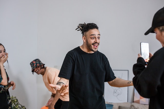 Uma senhora sorrindo e gravando dois rapazes e outra senhora para um vídeo.