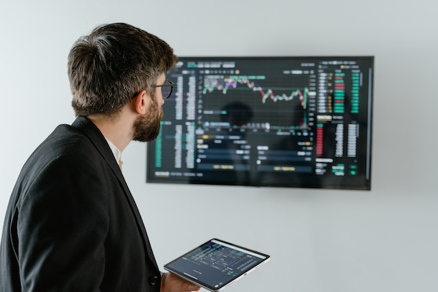 Um homem segurando um tablet preto e analisando dados em uma tela.