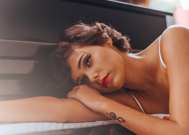 A woman with a sad look resting her head on a piano.