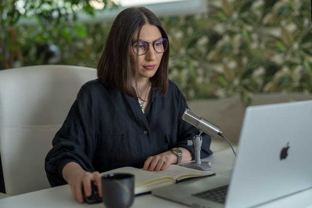 Een vrouw zit voor een laptop en microfoon. 