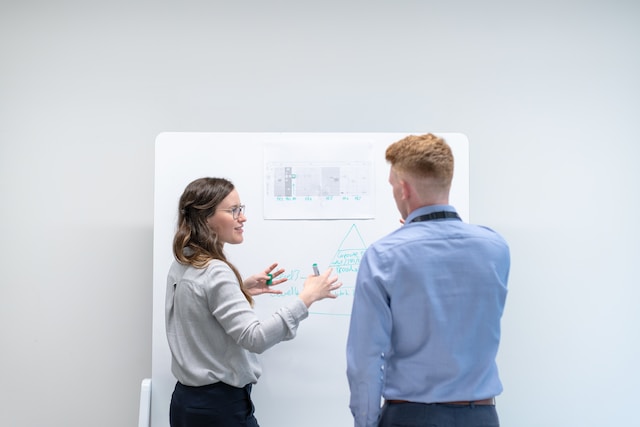 A man and a woman discussing in front of a whiteboard. 