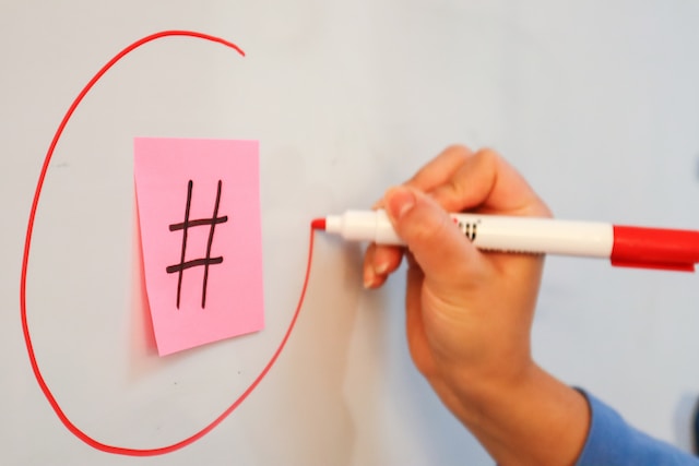 Eine Person zeichnet einen Kreis um ein Hashtag-Symbol auf ein Post-it, das auf einer Tafel klebt.