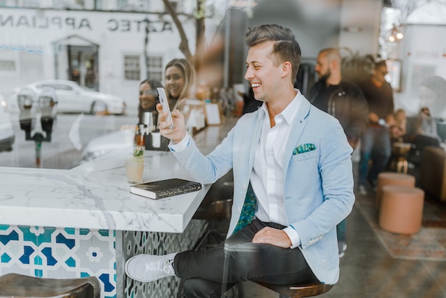 Un uomo sorridente seduto che utilizza il suo dispositivo mobile.