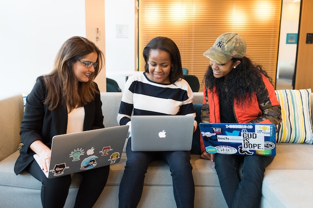 Three women having a discussion and using their laptops.