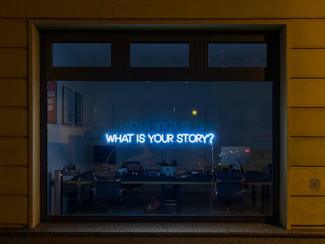 Un'insegna elettrica su una finestra che recita: "Qual è la tua storia?".