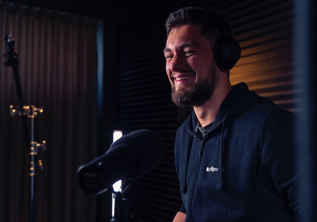 A man wearing headphones and sitting in front of a microphone in a sound studio.