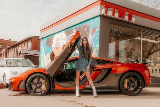 Een vrouwelijk model poseert naast een rode sportwagen. 