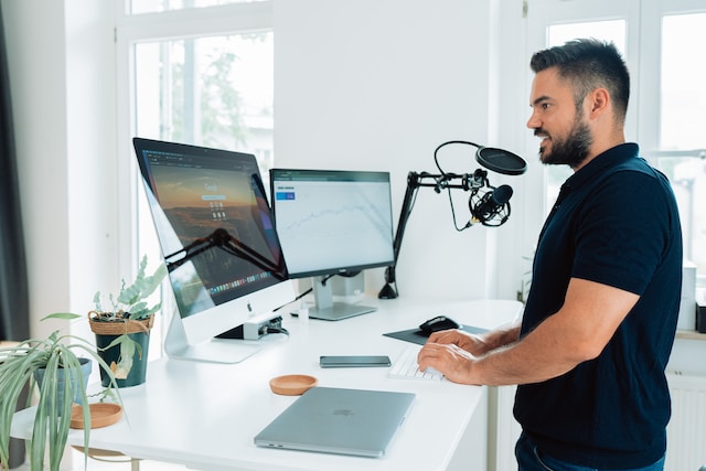 Um homem em frente a telas de computador e um microfone. 