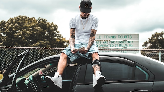 A man sitting on top of a car while counting money. 