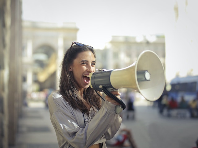 A woman screaming joyfully into a megaphone.