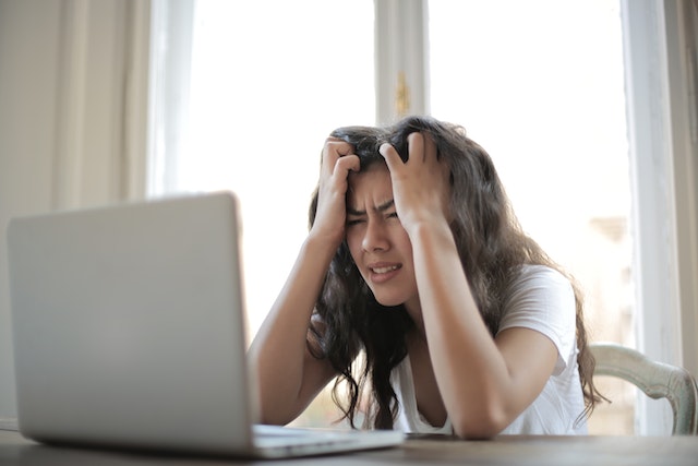 Eine Frau sitzt vor ihrem Laptop und zeigt ihre Frustration. 