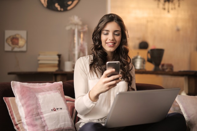 Uma mulher olhando para o telefone com o PC à sua frente.