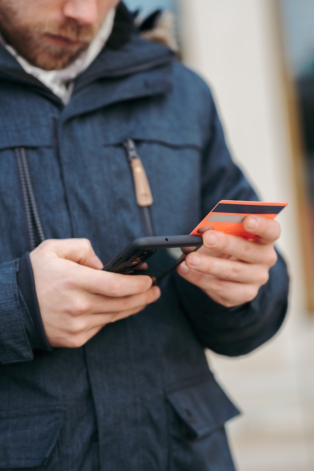 Ein Mann hält ein Telefon in der einen Hand und eine Kreditkarte in der anderen, um Tiktok zu kaufen.