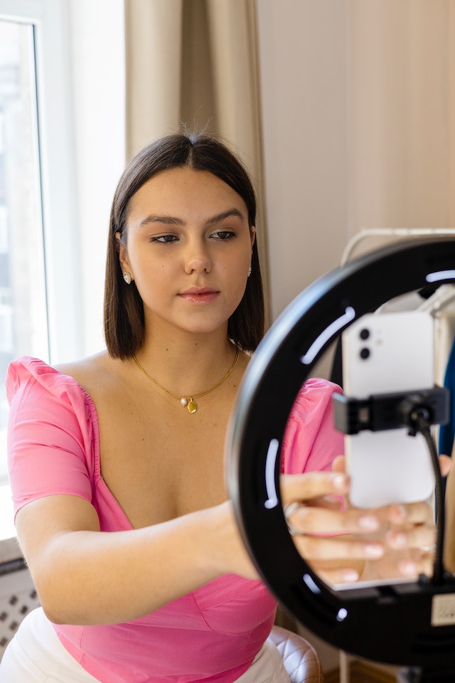 A girl in a pink blouse recording a TikTok.