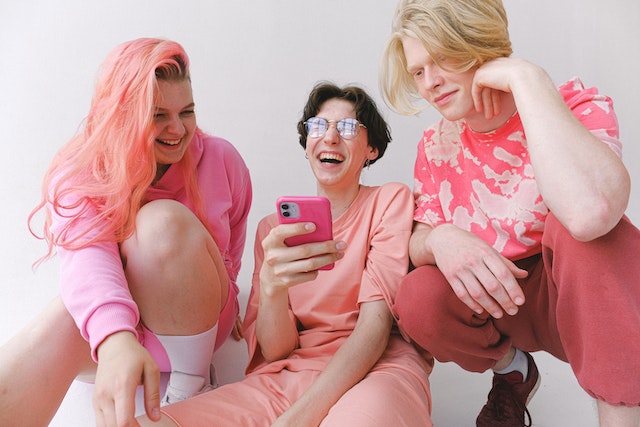 분홍색 옷을 입은 세 사람이 휴대폰을 보며 웃고 있습니다.