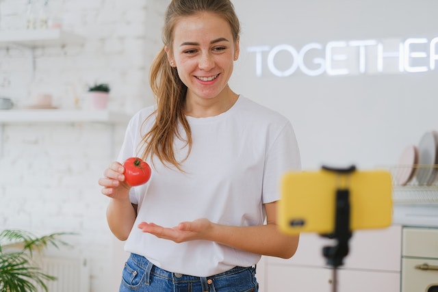 Uma jovem segurando um tomate e transmitindo ao vivo em seu telefone.