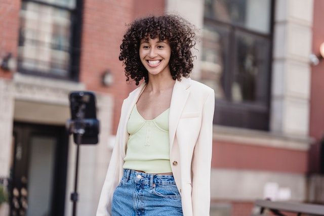 A young woman in a white jacket making a video of herself via her smartphone.