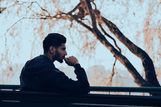 Un homme en sweat à capuche noir dans la rue, assis et réfléchissant.